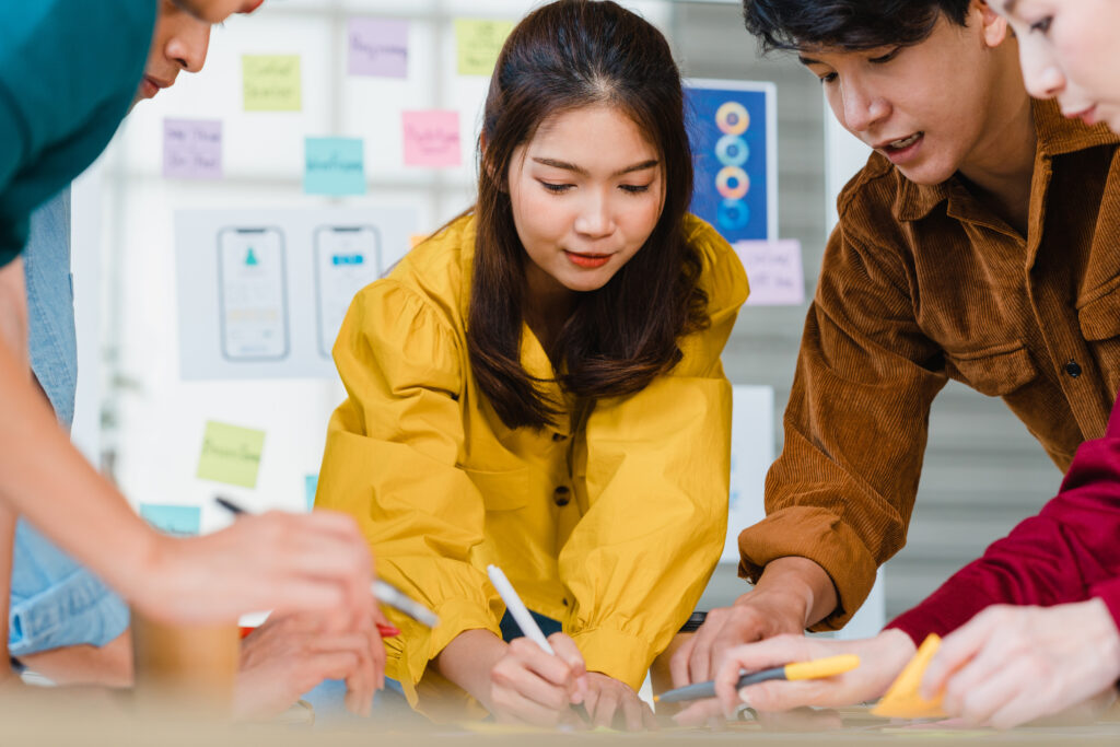 Team of young Asian professionals brainstorming ideas together during an active learning workshop in a modern office setting.
